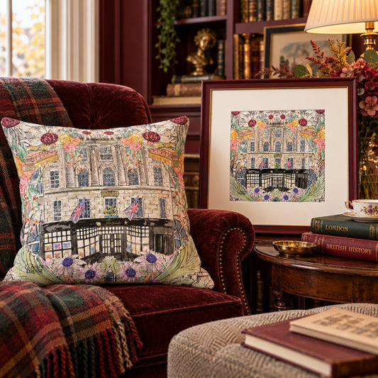 Hatchards In Full Bloom cushion on a burgundy armchair beside a matching framed print and books in a warmly lit reading nook.