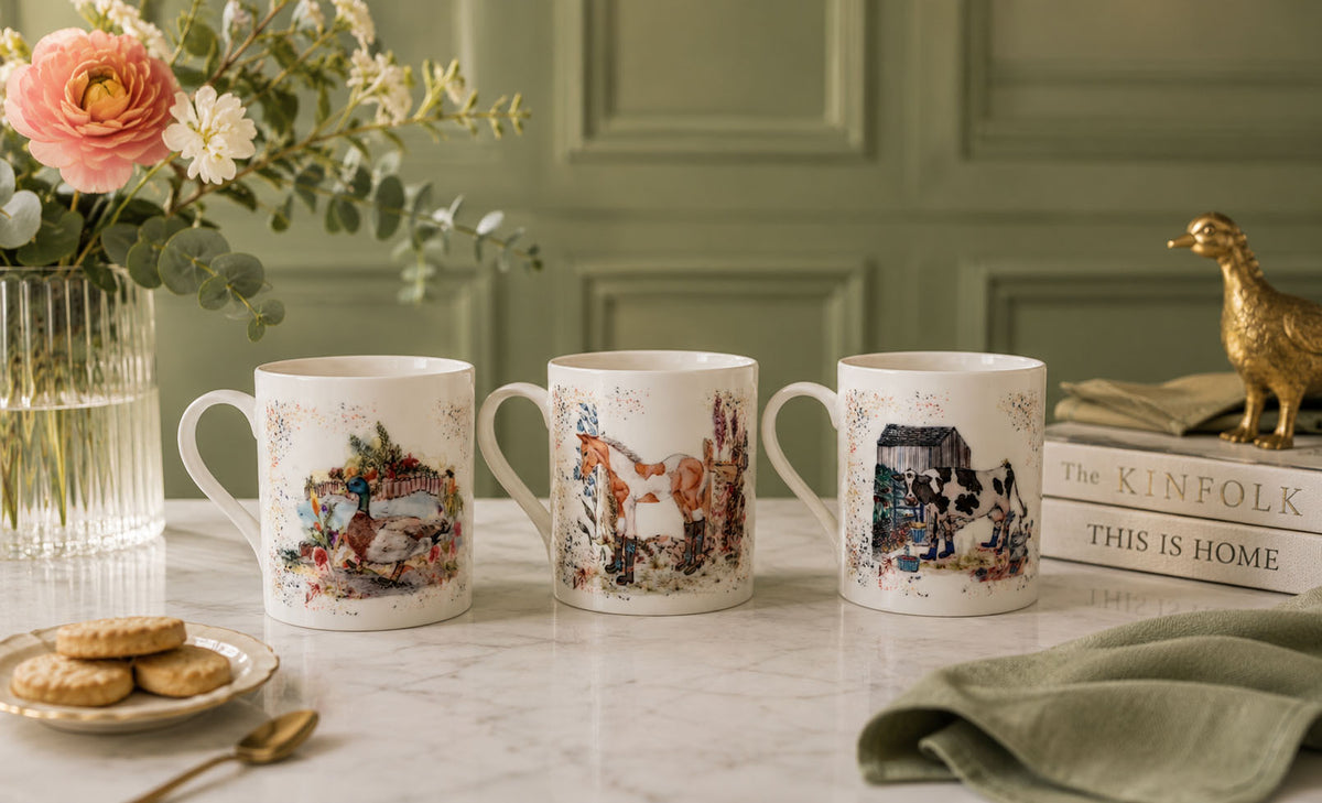 Three decorative mugs on a table with a floral arrangement and books in the background.