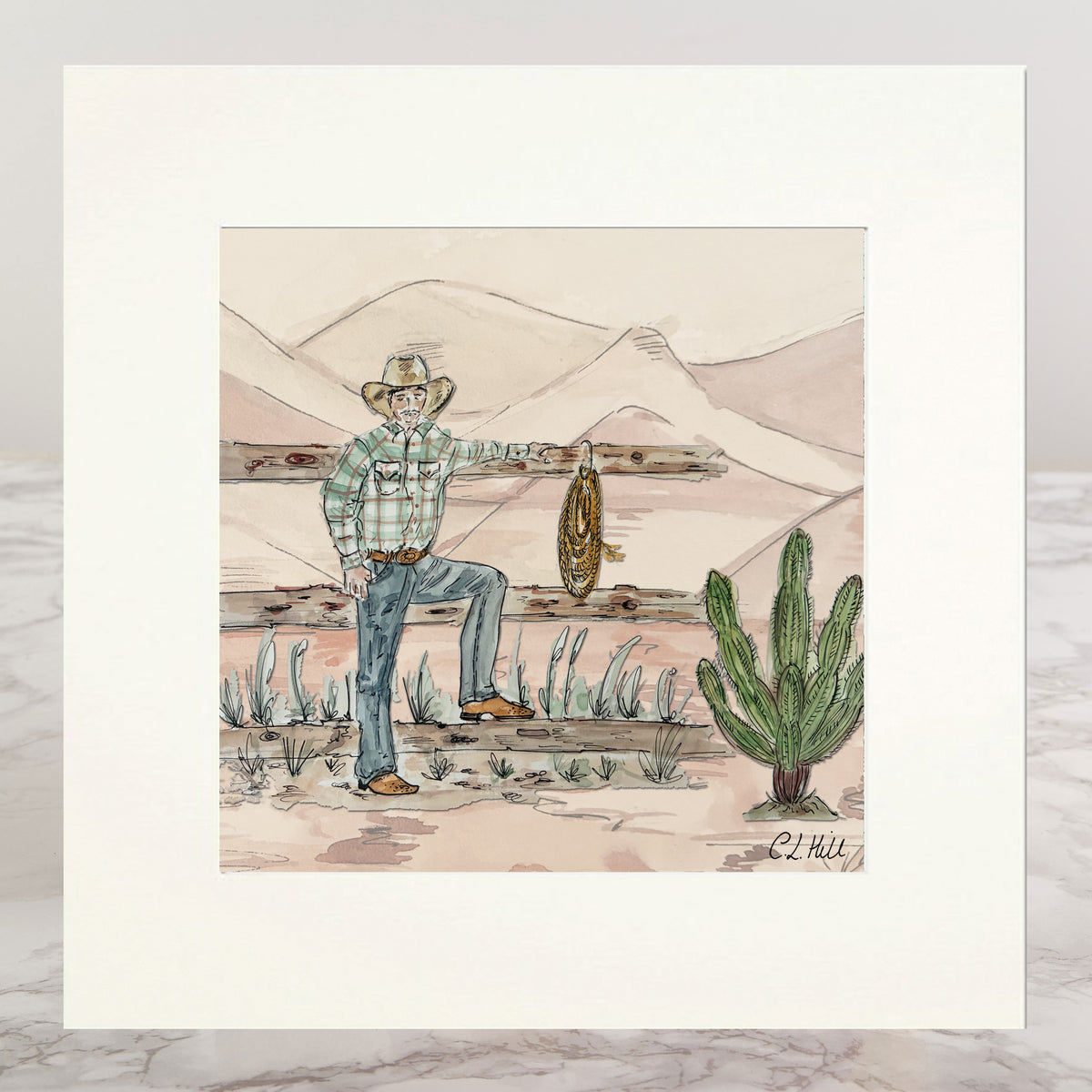 A matted art print featuring a hand-drawn western illustration of a cowboy in a plaid shirt and jeans, holding a lasso, with mountains, a fence, and a cactus in the background.