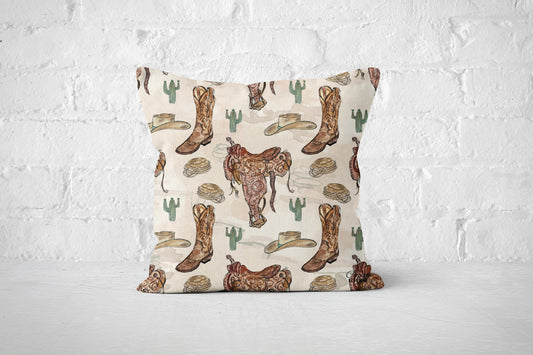 A square throw pillow with a western-themed print featuring brown cowboy boots, a brown steer, green cacti, and beige hats on a cream background, set against a white brick wall backdrop.