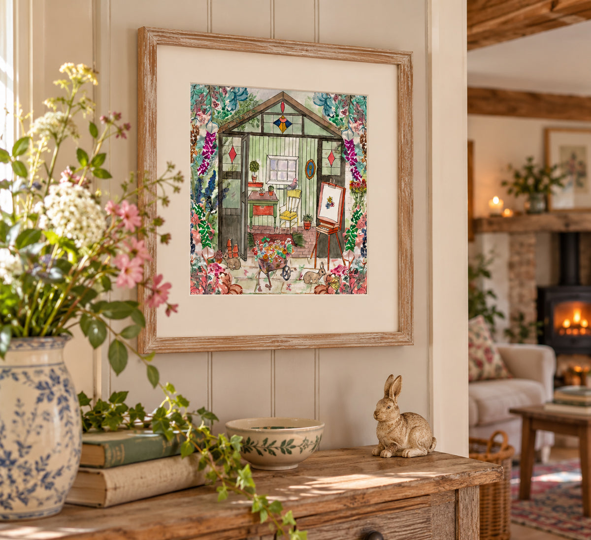 A framed art print depicting a whimsical garden greenhouse scene with colorful flowers and characters, styled on a wooden console table in a cozy, sunlit living room.