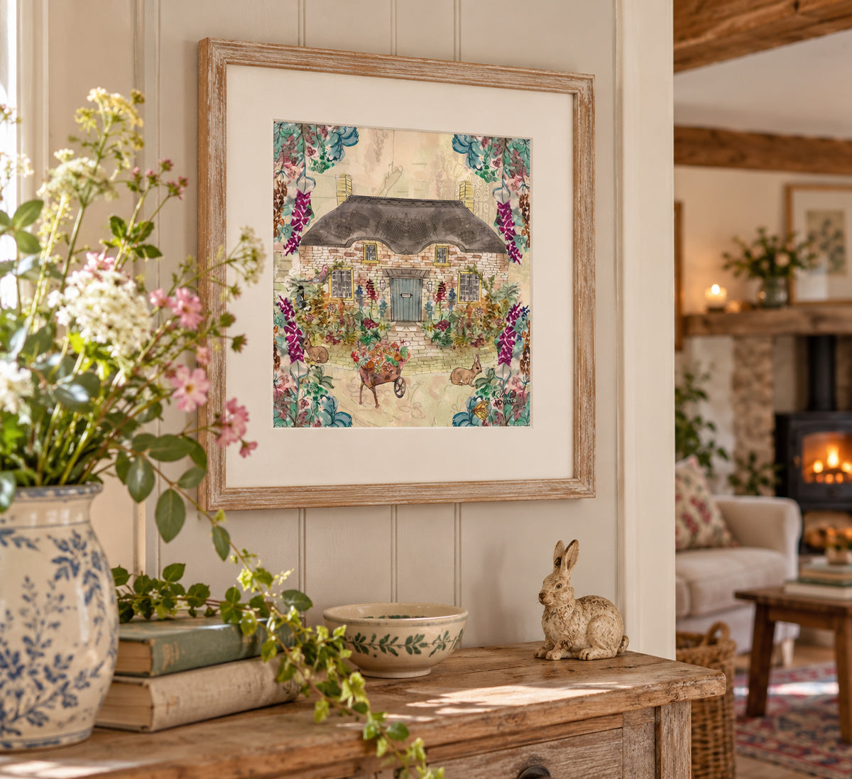 A framed art print depicting a cozy cottage scene with a horse-drawn carriage, displayed on a wooden console table in a warm, rustic living room setting.